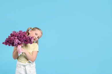 Photo of Little girl with bouquet of lilac flowers on light blue background, space for text