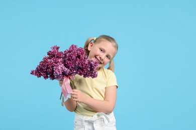 Photo of Little girl with bouquet of lilac flowers on light blue background