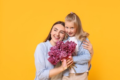 Photo of Mother and her daughter with bouquet of lilac flowers on yellow background