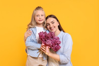 Photo of Mother and her daughter with bouquet of lilac flowers on yellow background