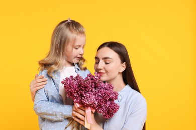 Photo of Mother and her daughter with bouquet of lilac flowers on yellow background