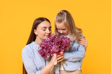 Photo of Mother and her daughter with bouquet of lilac flowers on yellow background