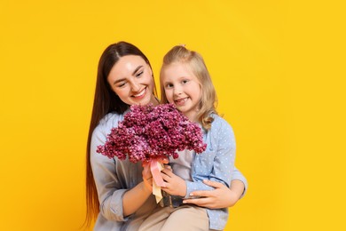 Photo of Mother and her daughter with bouquet of lilac flowers on yellow background