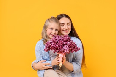 Photo of Mother and her daughter with bouquet of lilac flowers on yellow background