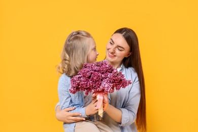 Photo of Mother and her daughter with bouquet of lilac flowers on yellow background