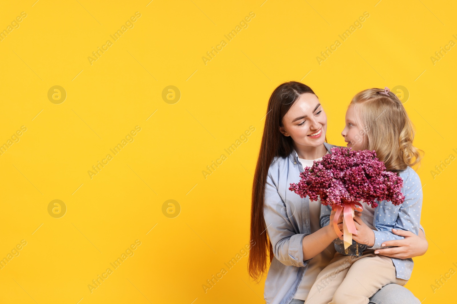 Mother and her daughter with bouquet of lilac flowers on yellow background, space for text Photo of Mother and her daughter with bouquet of lilac flowers on yellow background, space for text