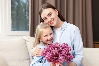 Photo of Mother and her daughter with bouquet of lilac flowers at home