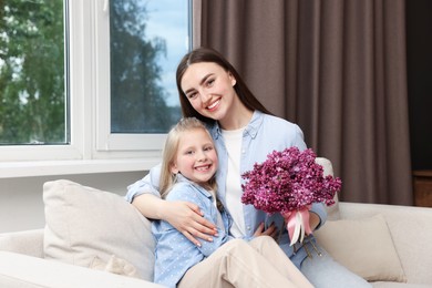 Photo of Mother and her daughter with bouquet of lilac flowers at home