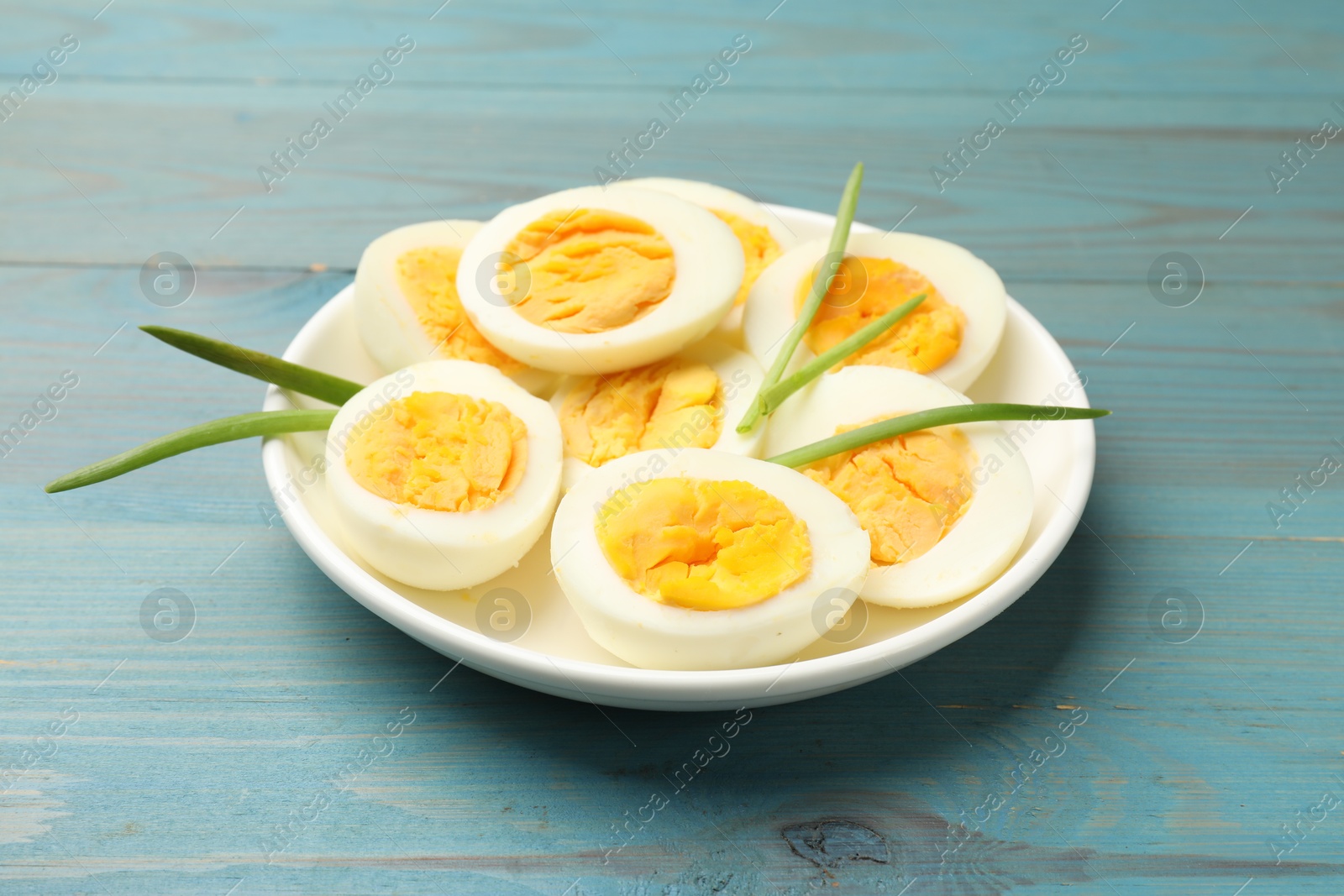 Halves of hard boiled eggs with green onions on blue wooden table Photo of Halves of hard boiled eggs with green onions on blue wooden table