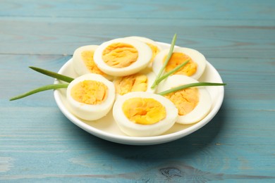 Photo of Halves of hard boiled eggs with green onions on blue wooden table