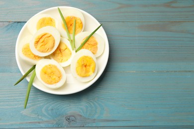 Photo of Halves of hard boiled eggs with green onions on blue wooden table, top view. Space for text