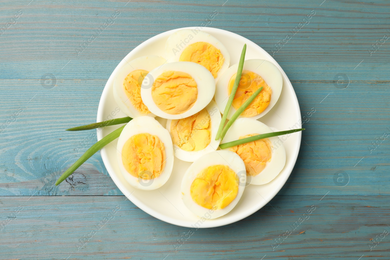 Halves of hard boiled eggs with green onions on blue wooden table, top view Photo of Halves of hard boiled eggs with green onions on blue wooden table, top view