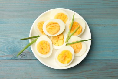Photo of Halves of hard boiled eggs with green onions on blue wooden table, top view