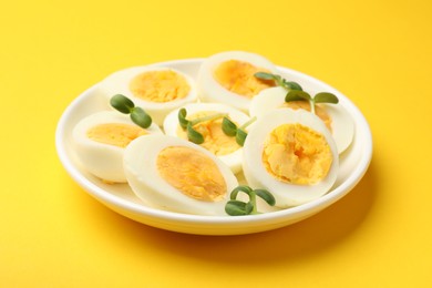 Photo of Halves of hard boiled eggs with microgreens on yellow background, closeup