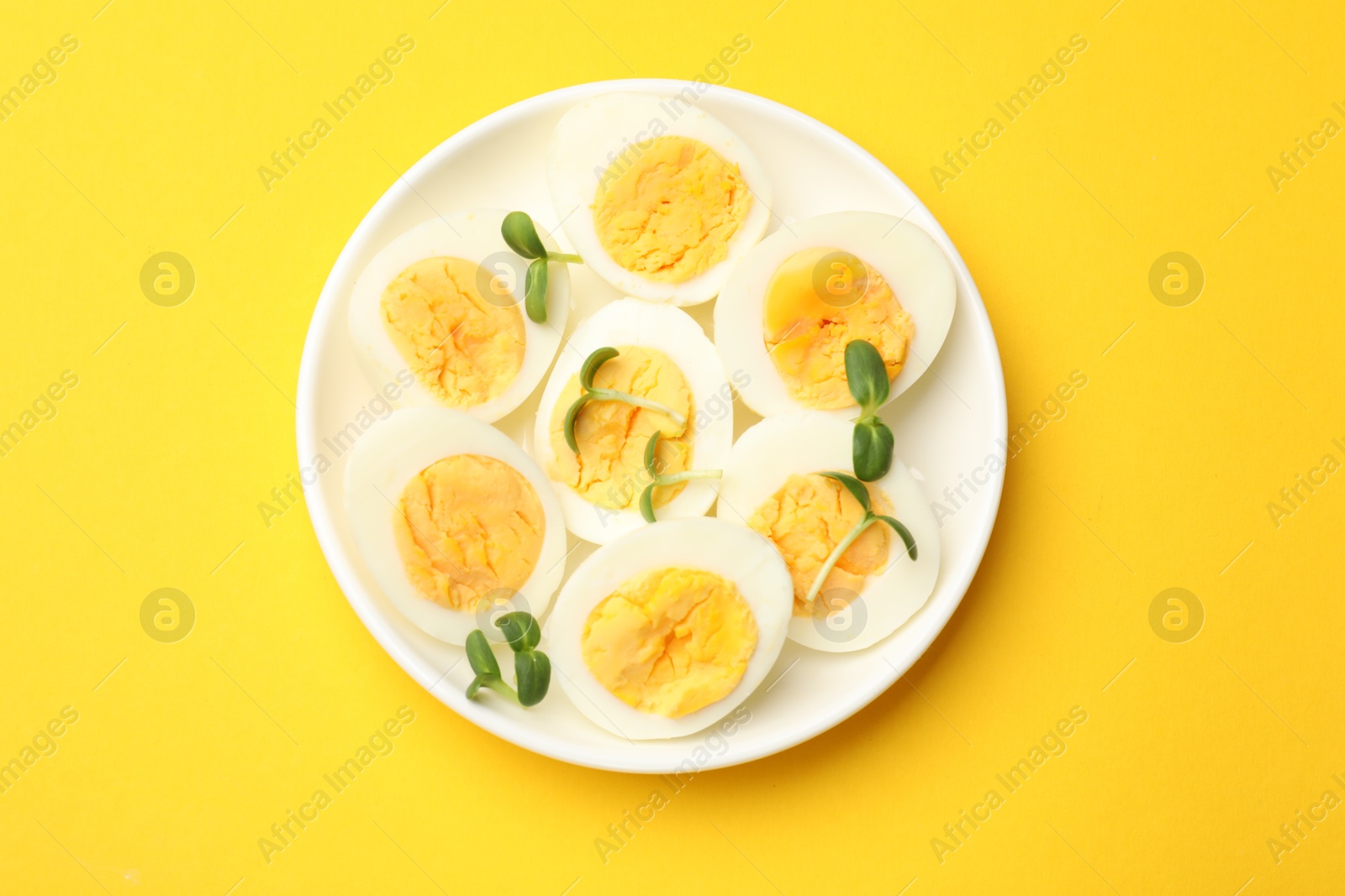 Photo of Halves of hard boiled eggs with microgreens on yellow background, top view