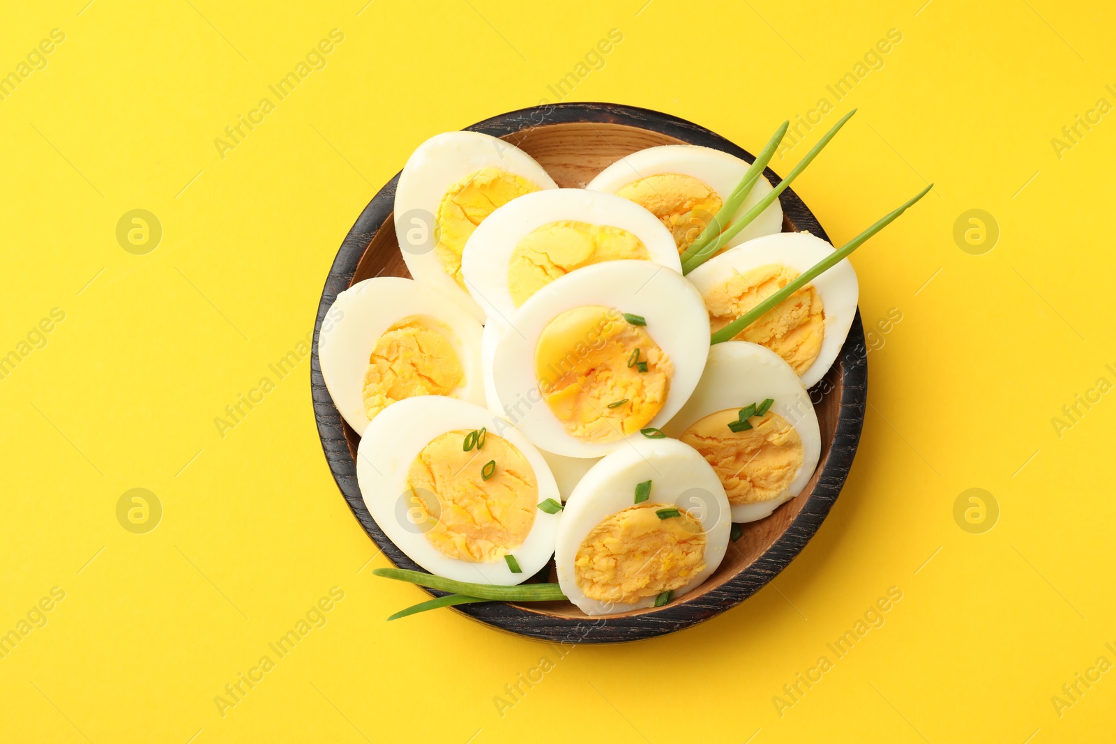 Halves of hard boiled eggs with green onions on yellow background, top view Photo of Halves of hard boiled eggs with green onions on yellow background, top view