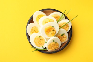 Photo of Halves of hard boiled eggs with green onions on yellow background, top view