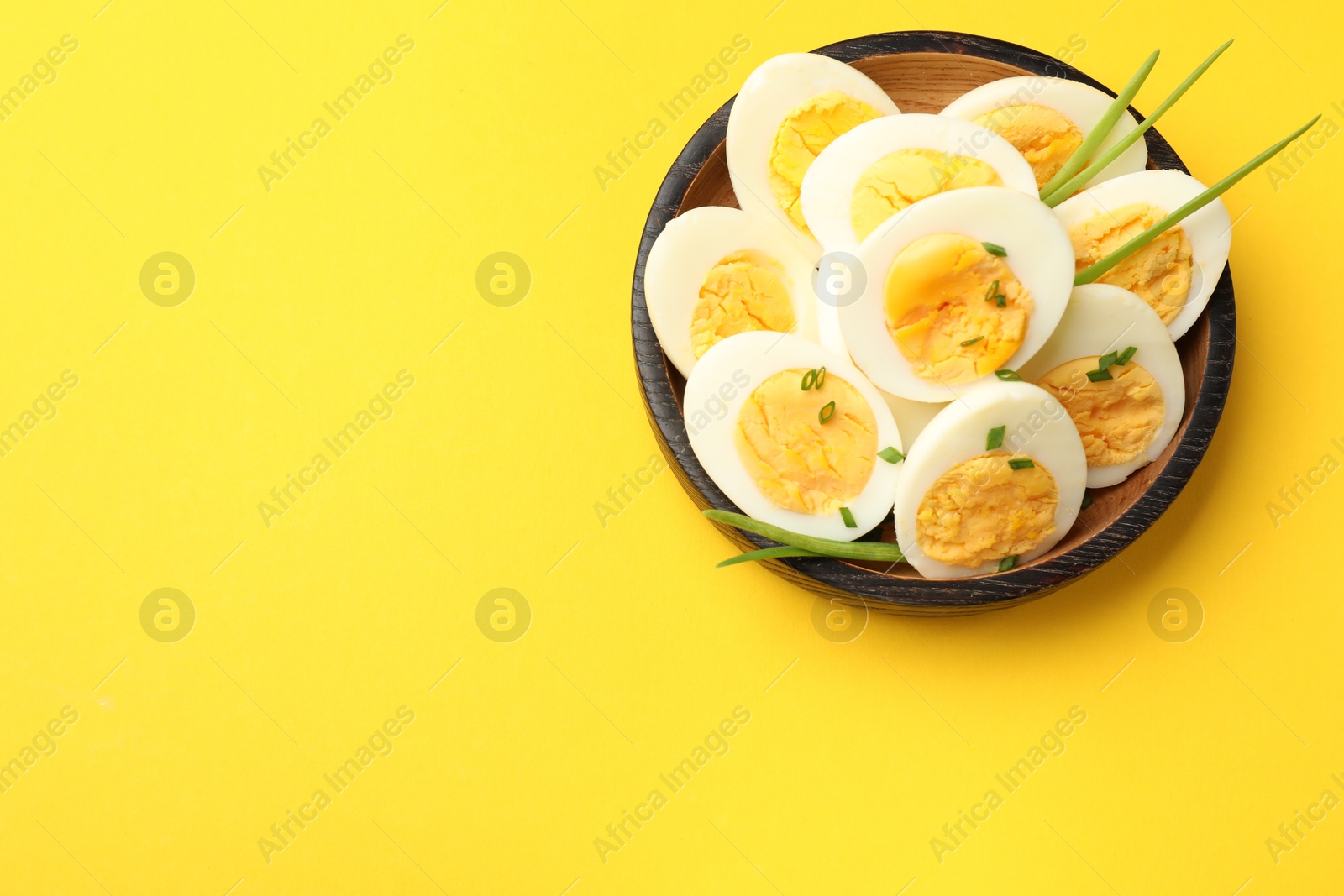 Halves of hard boiled eggs with green onions on yellow background, top view. Space for text Photo of Halves of hard boiled eggs with green onions on yellow background, top view. Space for text