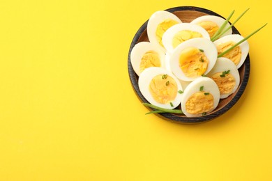 Photo of Halves of hard boiled eggs with green onions on yellow background, top view. Space for text