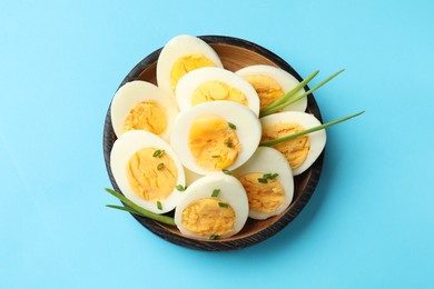 Photo of Halves of hard boiled eggs with green onions on light blue background, top view