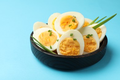 Photo of Halves of hard boiled eggs with green onions on light blue background, closeup