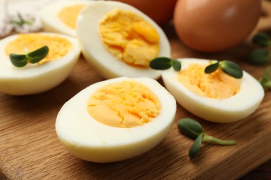 Photo of Halves of hard boiled eggs with microgreens on wooden table, closeup