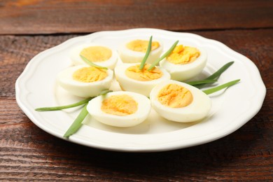 Photo of Halves of hard boiled eggs with green onions on wooden table, closeup