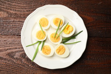 Photo of Halves of hard boiled eggs with green onions on wooden table, top view
