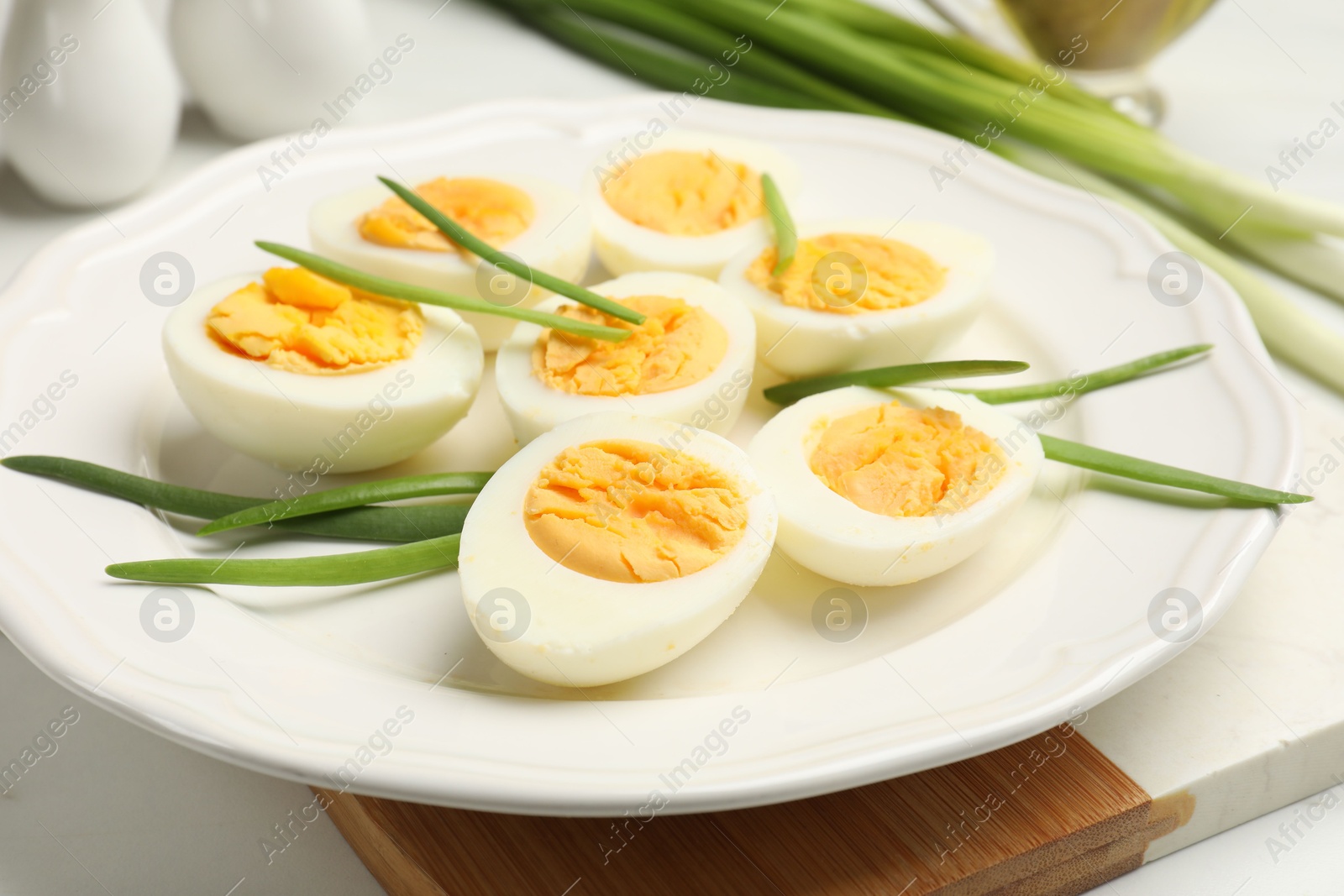 Photo of Halves of hard boiled eggs with green onions on white table, closeup