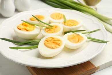 Photo of Halves of hard boiled eggs with green onions on white table, closeup