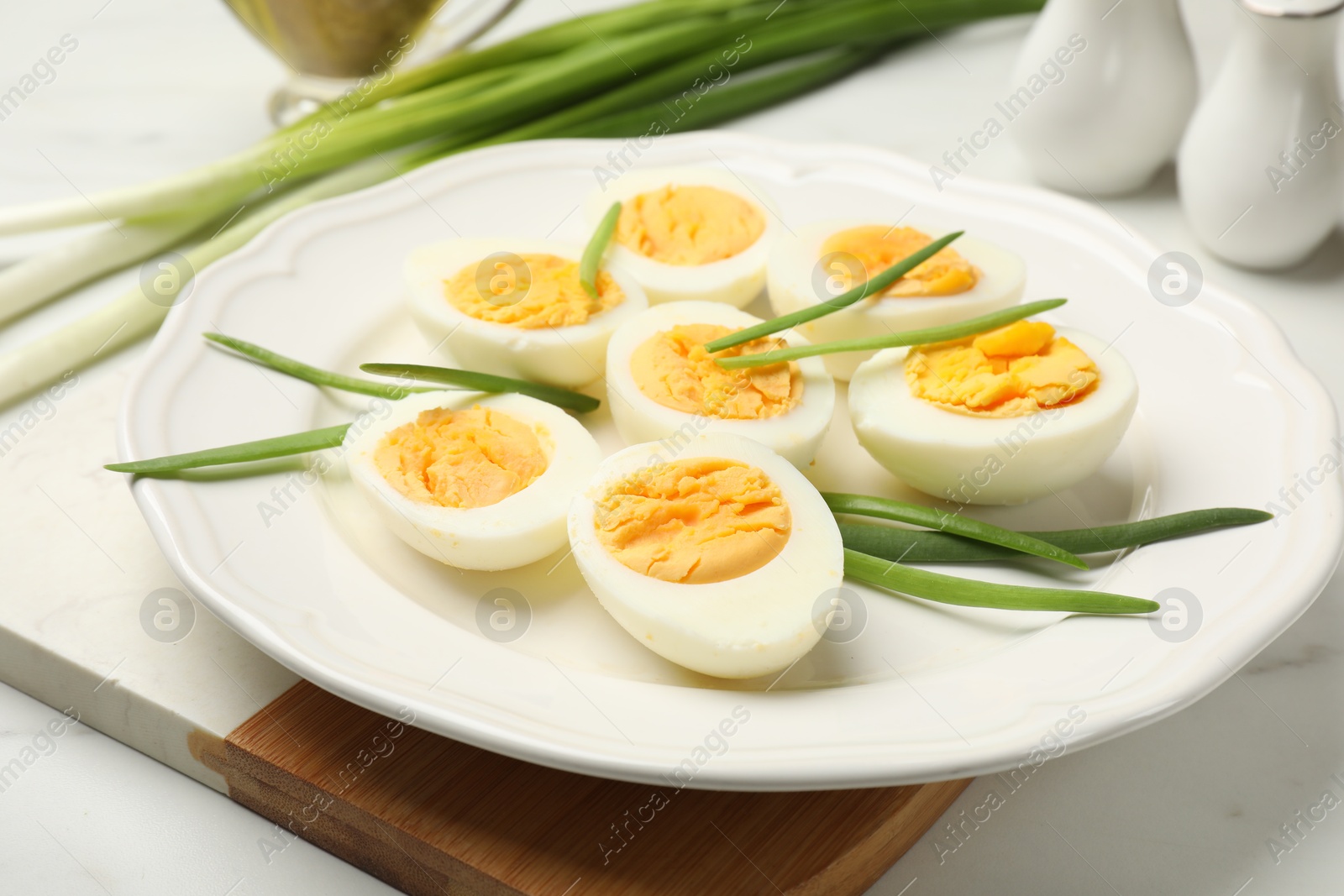 Halves of hard boiled eggs with green onions on white table, closeup Photo of Halves of hard boiled eggs with green onions on white table, closeup