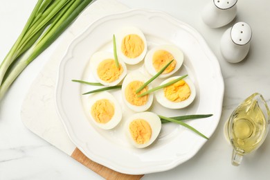 Photo of Halves of hard boiled eggs with green onions on white table, flat lay