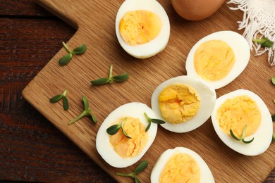 Photo of Halves of hard boiled eggs with microgreens on wooden table, top view