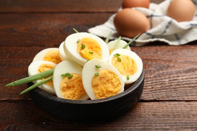 Photo of Halves of hard boiled eggs with green onions on wooden table, closeup