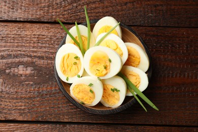 Photo of Halves of hard boiled eggs with green onions on wooden table, top view