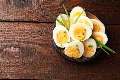 Photo of Halves of hard boiled eggs with green onions on wooden table, top view. Space for text