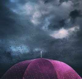 Image of Purple umbrella under cloudy sky, view through wet window. Stormy weather