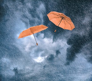 Image of Orange umbrellas flying in cloudy sky under heavy rain. Stormy weather