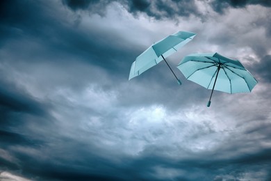 Image of Light blue umbrellas flying in cloudy sky. Stormy weather