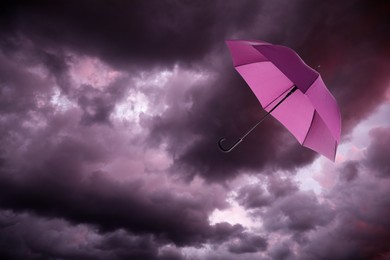 Image of Pink umbrella flying in dark cloudy sky. Stormy weather