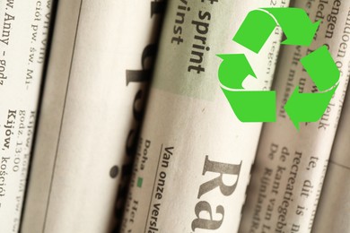 Image of Recycling symbol and many newspapers in different languages as background, closeup. Eco-friendly lifestyle, reusing
