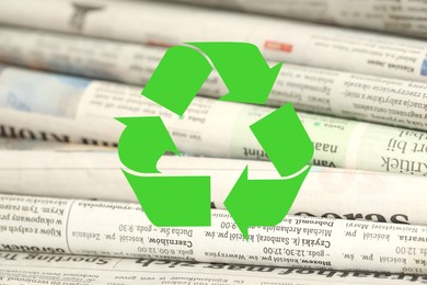 Image of Recycling symbol and many newspapers in different languages as background, closeup. Eco-friendly lifestyle, reusing