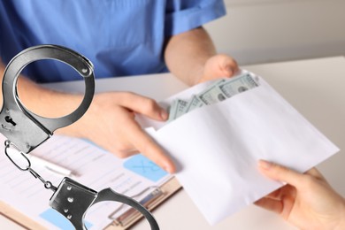 Image of Stop corruption. Doctor taking bribe from woman at table, closeup. Handcuffs symbolizing unlawful actions
