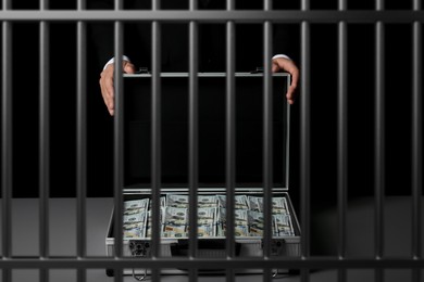 Image of Stop corruption. Man with suitcase full of money in jail, closeup. Imprisonment for bribery