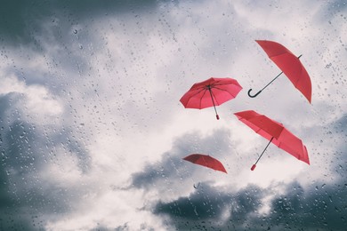 Image of Red umbrellas flying in cloudy sky, view through wet window. Stormy weather