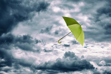 Image of Light green umbrella flying in cloudy sky. Stormy weather