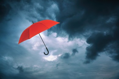 Image of Red umbrella flying in dark cloudy sky. Stormy weather