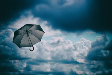 Image of Black umbrella flying in dark cloud sky. Stormy weather