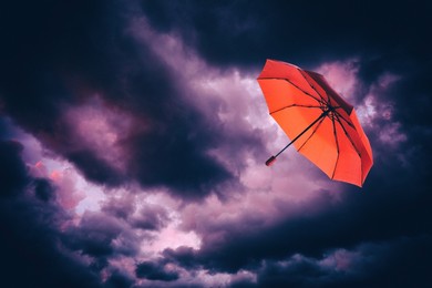 Image of Red umbrella flying in dark cloudy sky. Stormy weather