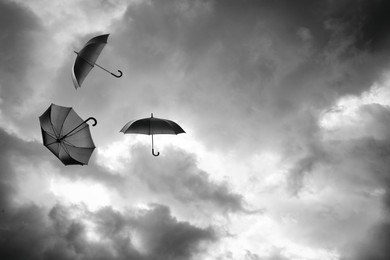 Image of Black umbrellas flying in cloudy sky. Stormy weather